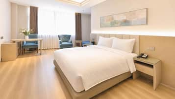 Quarto de hotel com cama, mesa de cabeceira, escrivaninha, cadeira e um quadro na parede.