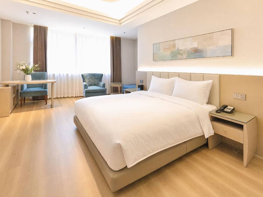 Quarto de hotel com cama, mesa de cabeceira, escrivaninha, cadeira e um quadro na parede.