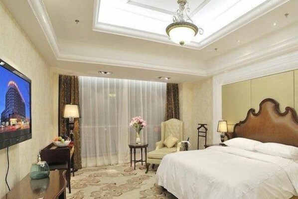 A hotel room with a bed, a television, a desk with a lamp, and a chair.