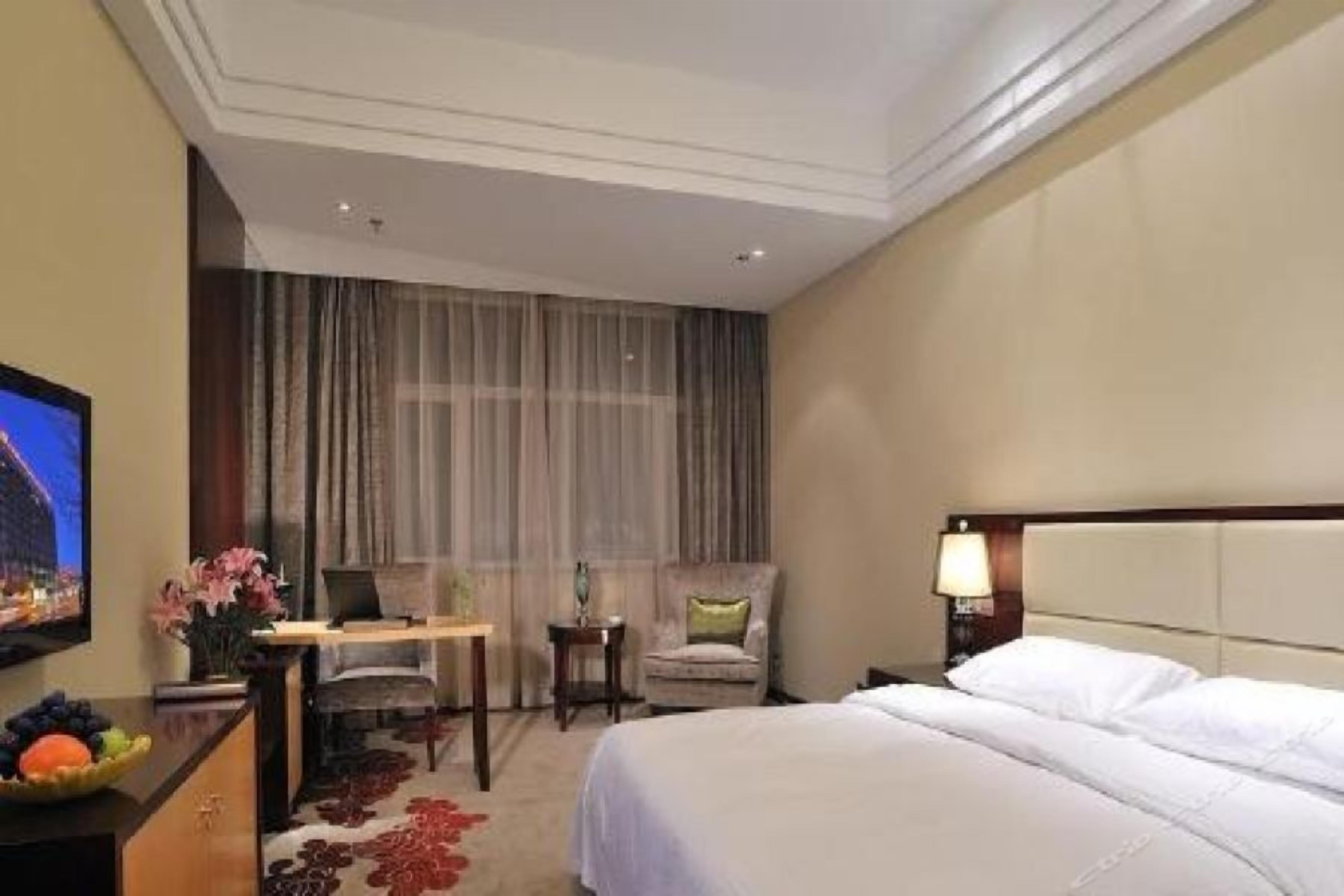 Habitación de hotel con cama, escritorio, silla, televisor y mesita de noche con lámpara.