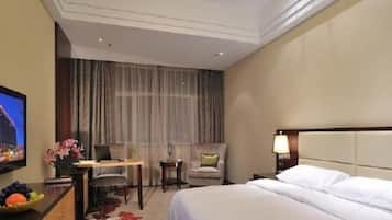 A hotel room with a bed, a desk, a chair, a television, and a nightstand with a lamp.