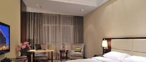 Habitación de hotel con cama, escritorio, silla, televisor y mesita de noche con lámpara.