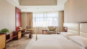 A hotel room with a large bed, a desk, a chair, a small table, and a TV.
