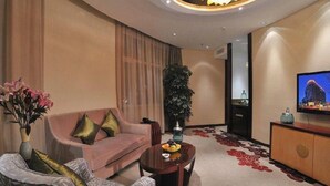Una habitación de hotel con sofá, mesa de centro, televisor y una planta grande.