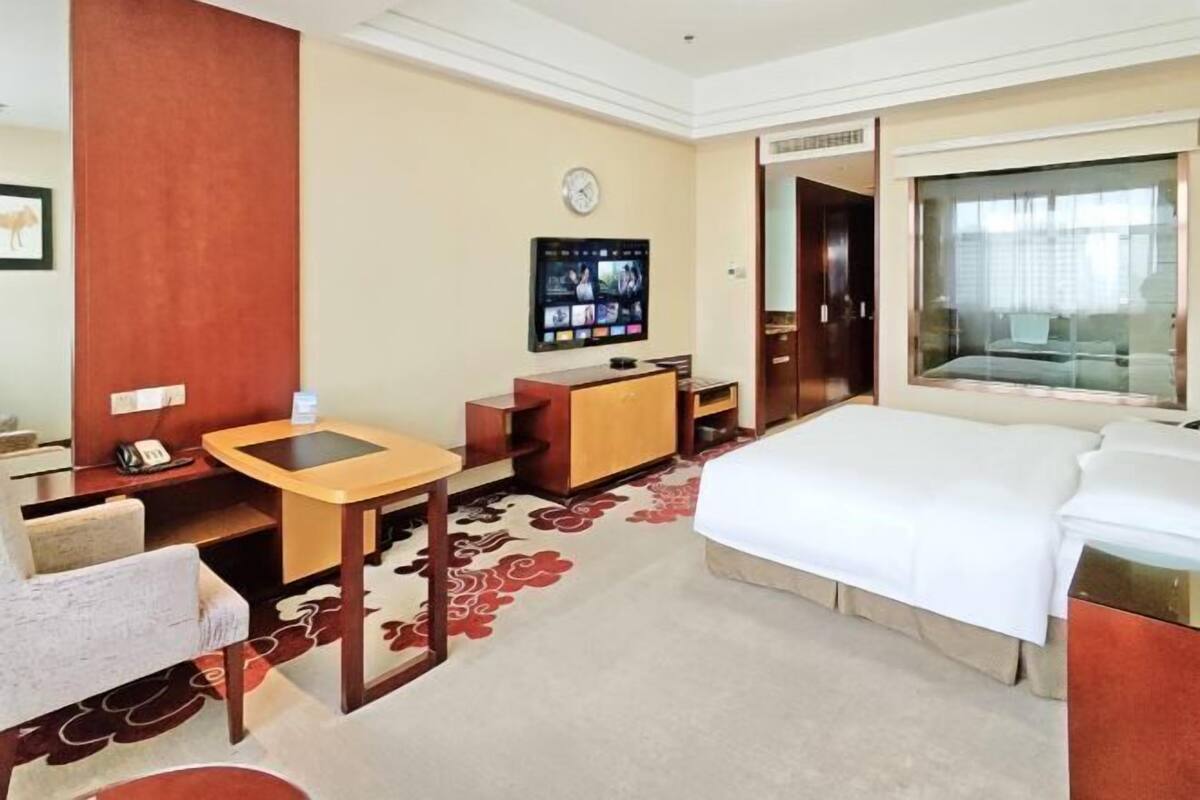 Une chambre d’hôtel avec un lit, un bureau, une chaise, une télévision et une fenêtre.