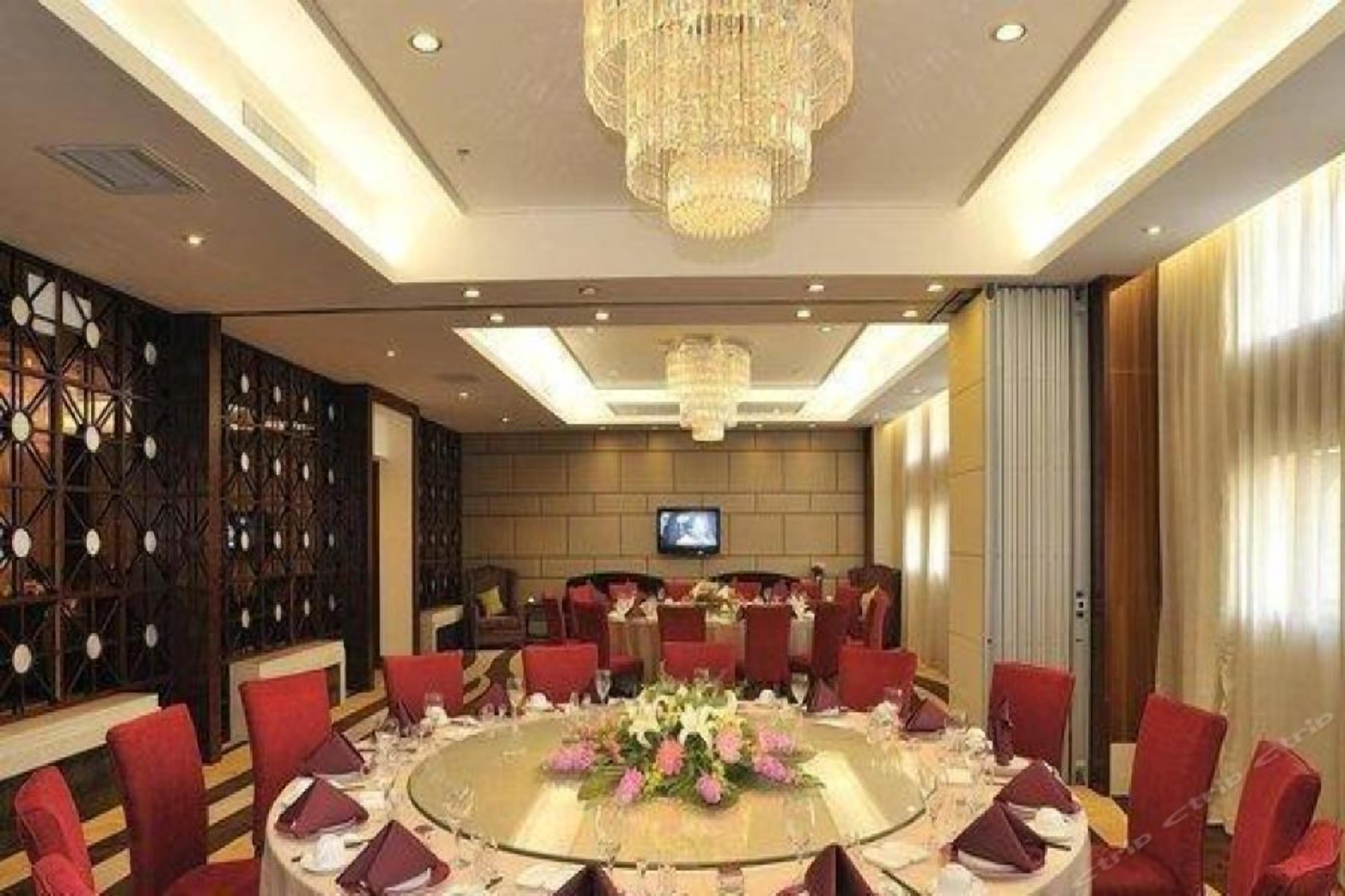 A conference room with a round table, red chairs, a chandelier, and a television screen.