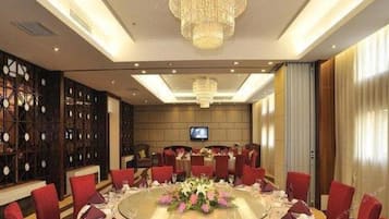 A conference room with a round table, red chairs, a chandelier, and a television screen.