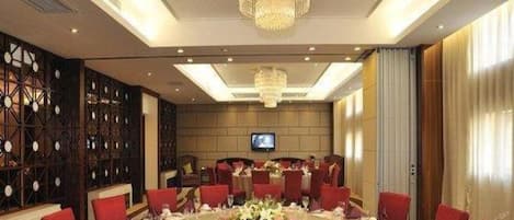 A conference room with a round table, red chairs, a chandelier, and a television screen.
