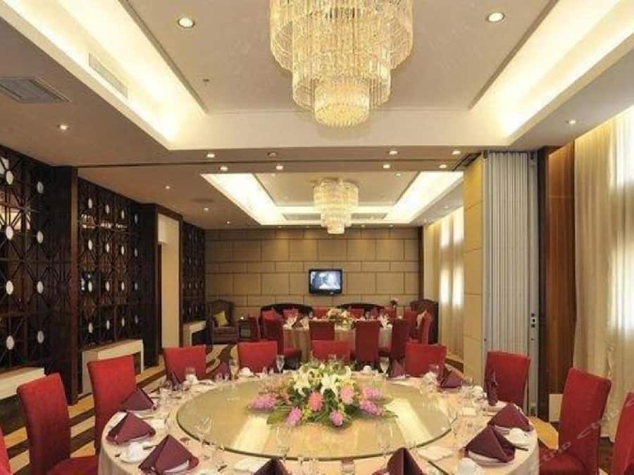 A conference room with a round table, red chairs, a chandelier, and a television screen.