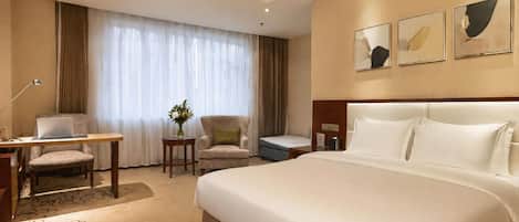 A hotel room with a large bed, two chairs, a desk, and a small table.