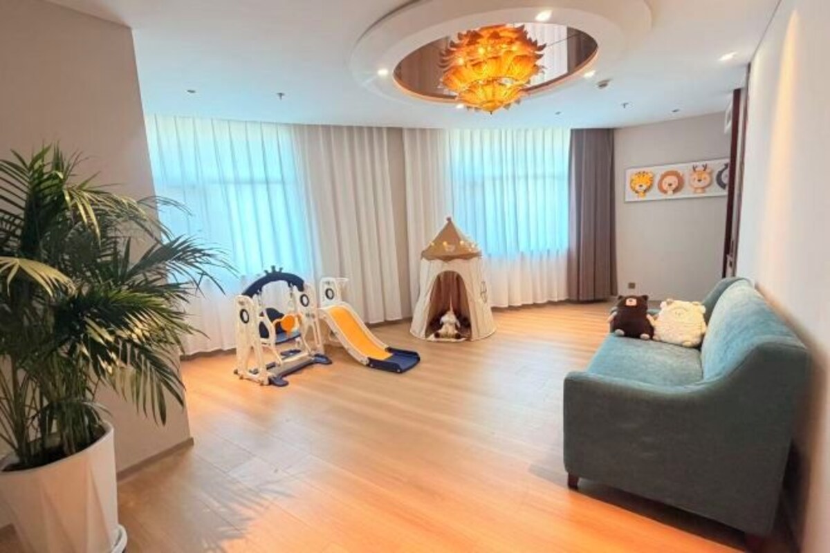 A living room with a play area, a sofa, a potted plant, and a chandelier.
