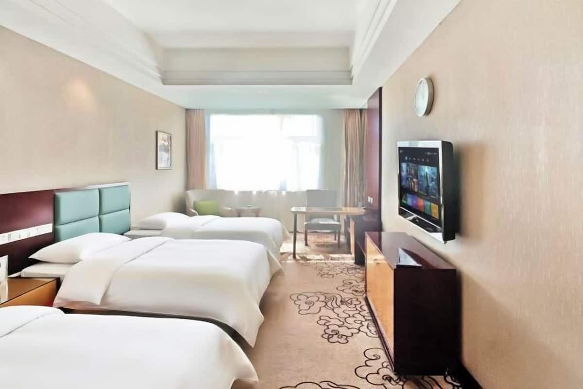 Une chambre d’hôtel avec deux lits, un bureau, une chaise, une télévision et une fenêtre.