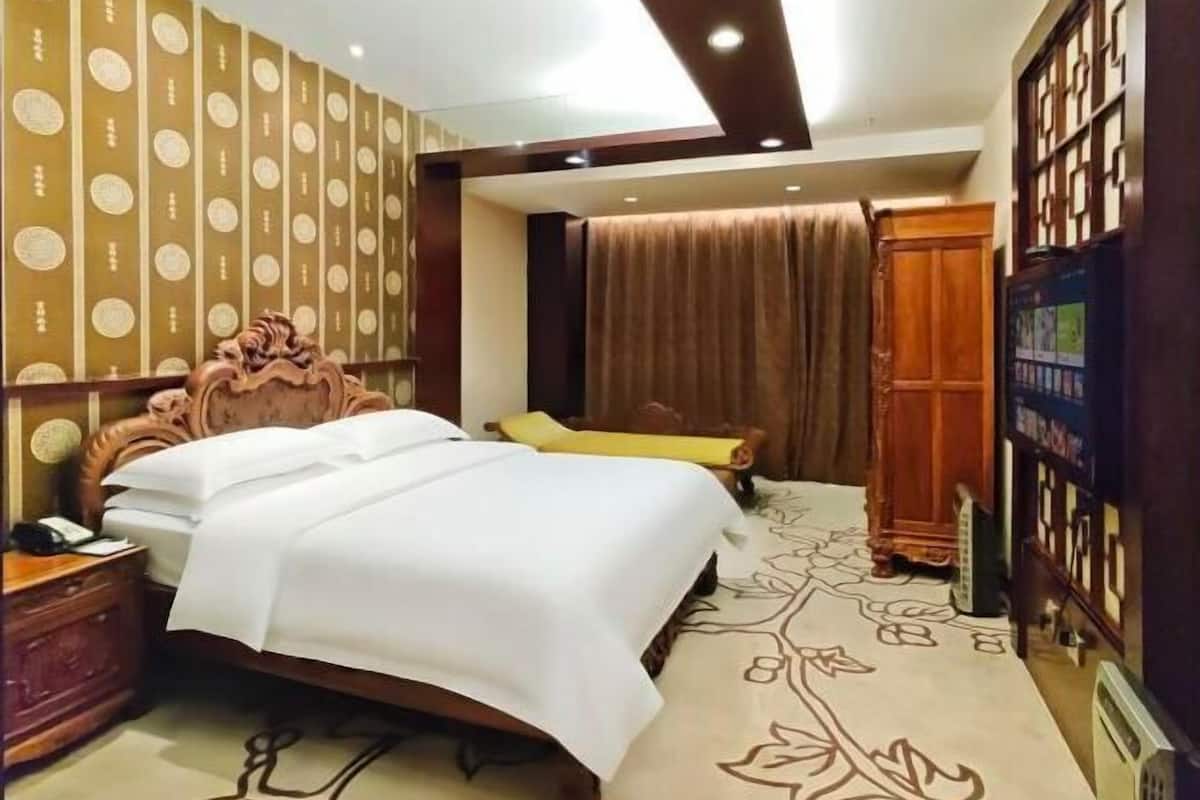 A hotel room with a large bed, a wooden headboard, a nightstand, a television, and a wardrobe.
