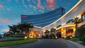 A Sheraton hotel with a curved glass facade, palm trees, and well-lit entrance. - Sheraton Fuzhou Hotel (Fuzhou)