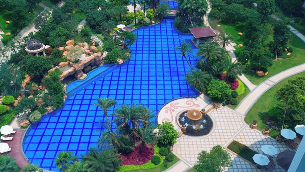 An aerial view of a resort with a large blue pool, palm trees, and a circular fountain area. - Sheraton Fuzhou Hotel (Fuzhou)