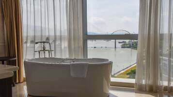 A modern bathroom with a freestanding bathtub, a towel, and a view of a bridge and water body through large windows.