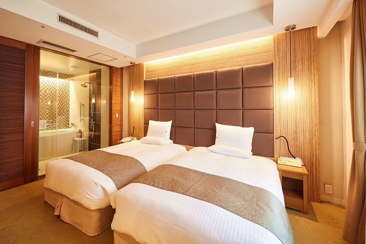 Quarto de hotel com uma cama grande, banheiro separado e cabeceira de madeira.