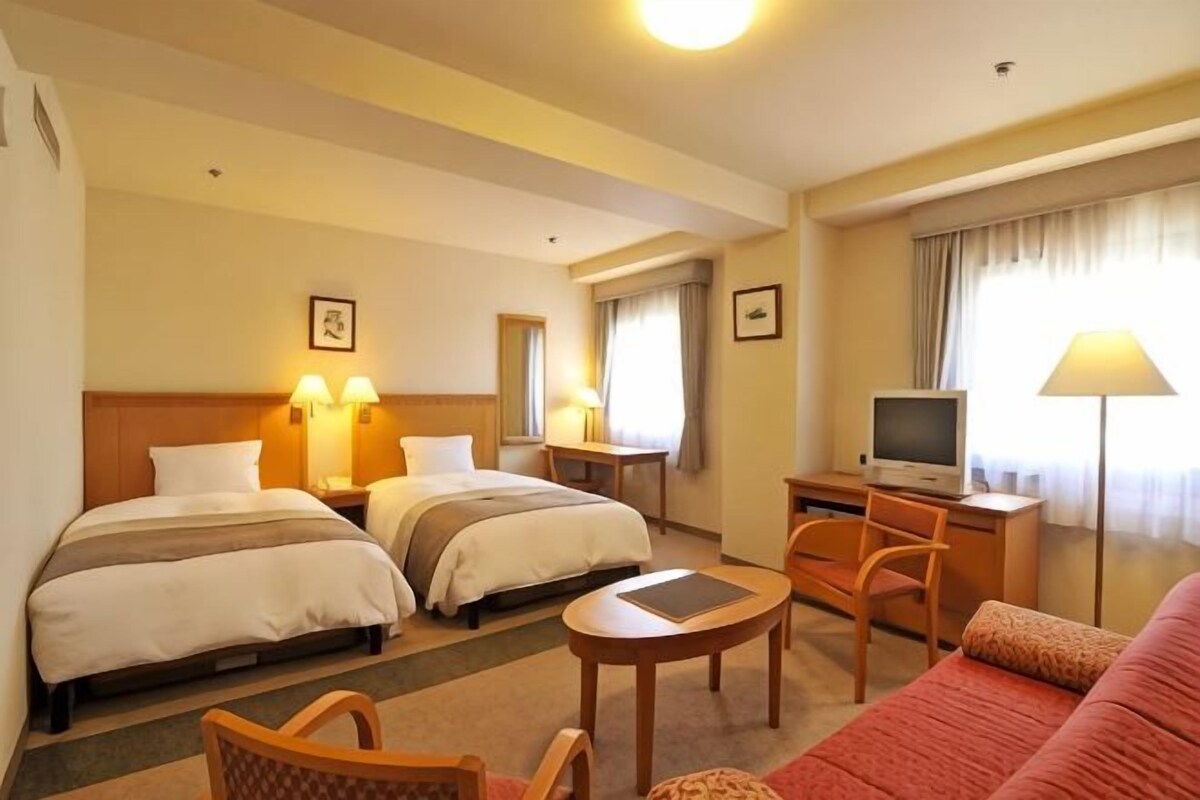 A hotel room with two beds, a desk with a computer, a TV, a sofa, and a small table.