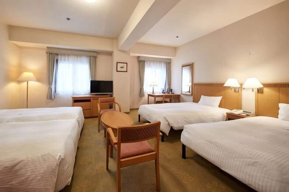 Quarto de hotel com quatro camas, uma escrivaninha, uma televisão e duas luminárias.