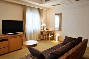 Habitación de hotel con televisor de pantalla plana, un escritorio de madera, una silla, una mesa de centro redonda, un sofá y un espejo en la pared.
