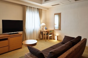 Habitación de hotel con televisor de pantalla plana, un escritorio de madera, una silla, una mesa de centro redonda, un sofá y un espejo en la pared.