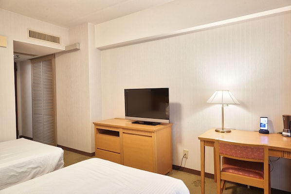 Habitación de hotel con dos camas, un escritorio con televisor, una lámpara y una estación de carga para teléfono.