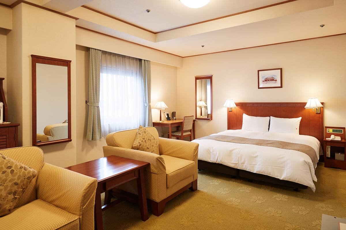 Quarto de hotel com cama, sofá, escrivaninha e cadeira.