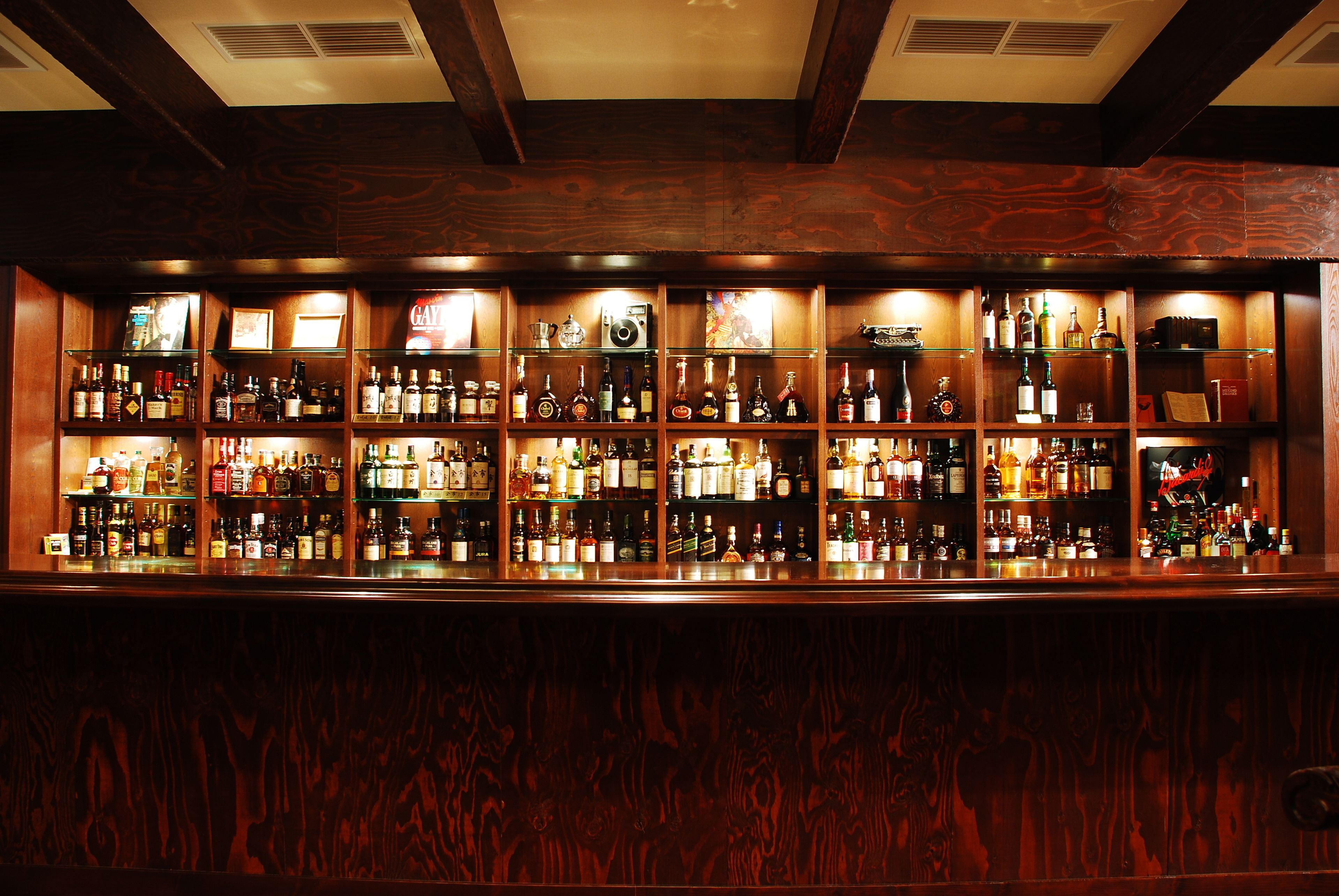 A bar with multiple shelves of liquor bottles and glasses, wooden paneling, and a ceiling with exposed beams.