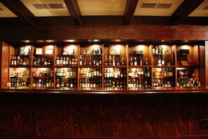 A bar with multiple shelves of liquor bottles and glasses, wooden paneling, and a ceiling with exposed beams. - Pacific Hotel Okinawa (Naha)