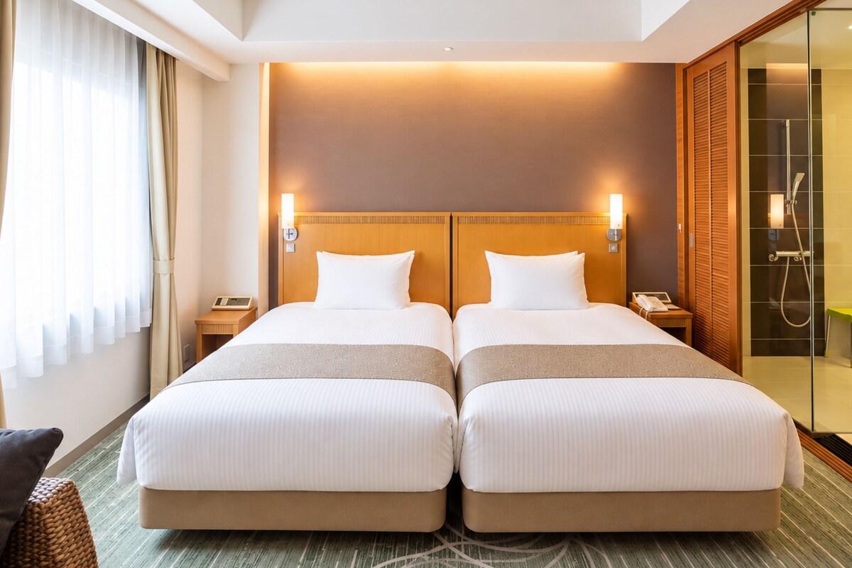 A hotel room with two beds, a glass shower enclosure, and a bedside table with a phone.