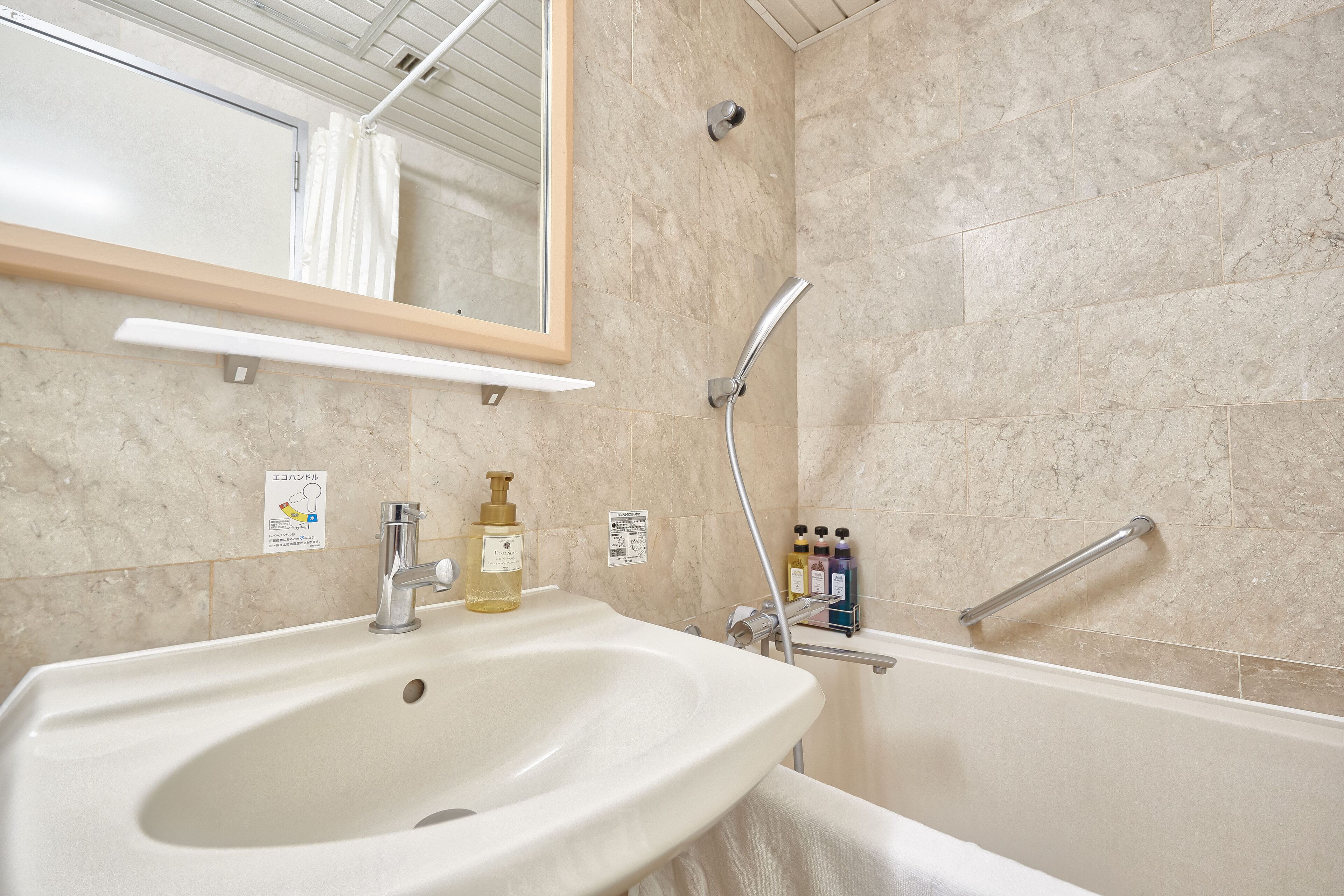 Baño con lavamanos, espejo, ducha y toallero.