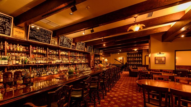 A bar area with wooden furniture, a long counter with bottles, and a patterned carpet. - Pacific Hotel Okinawa (Naha)