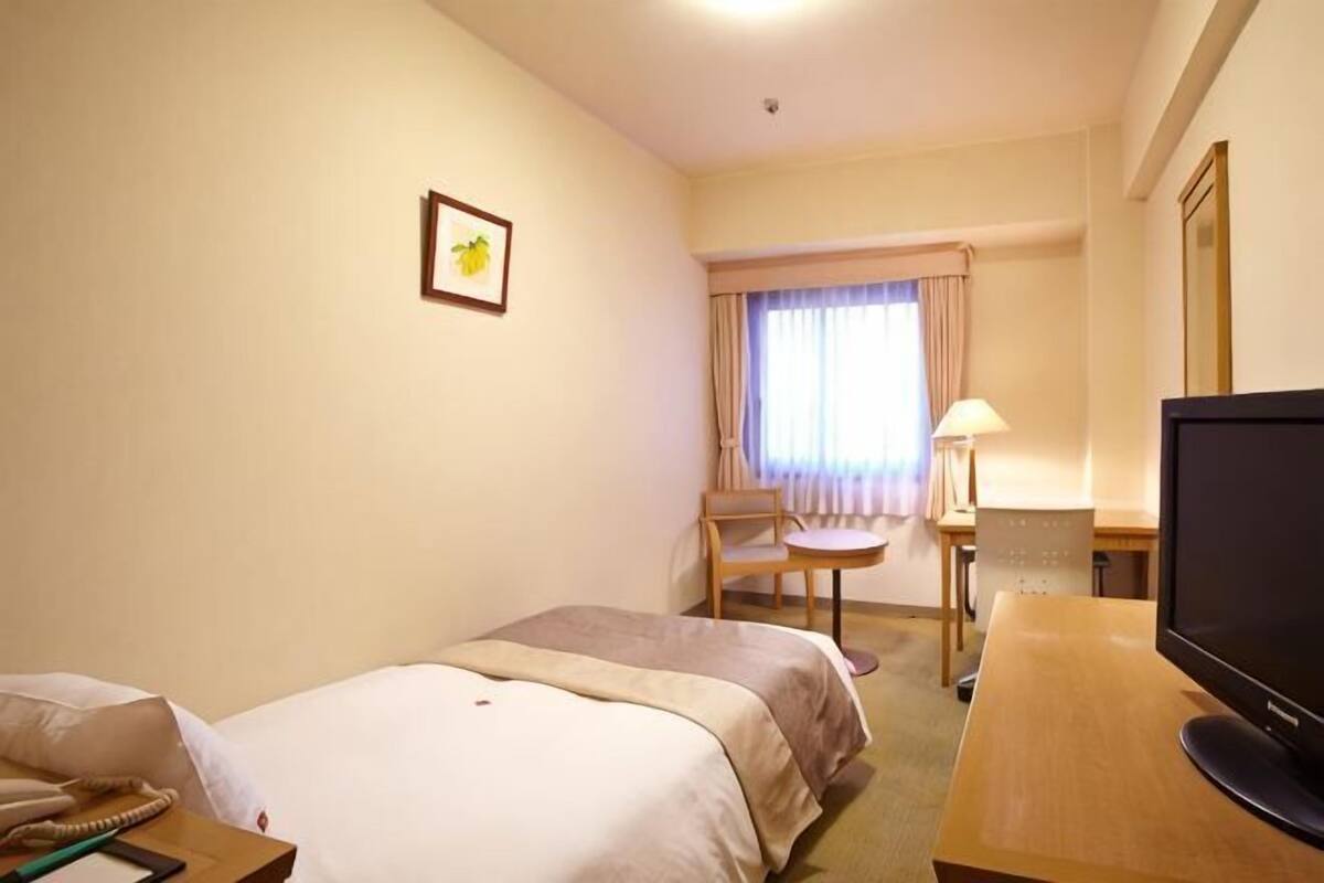 A hotel room with two beds, a desk with a TV, a chair, a lamp, and a window with curtains.