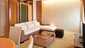 A modern living room with a sectional sofa, a glass coffee table, and a small ottoman. - Pacific Hotel Okinawa (Naha)