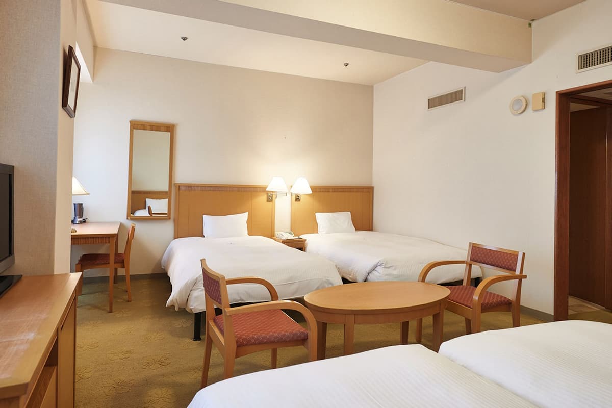 Quarto de hotel com duas camas, uma escrivaninha, uma cadeira, uma mesa e uma televisão.