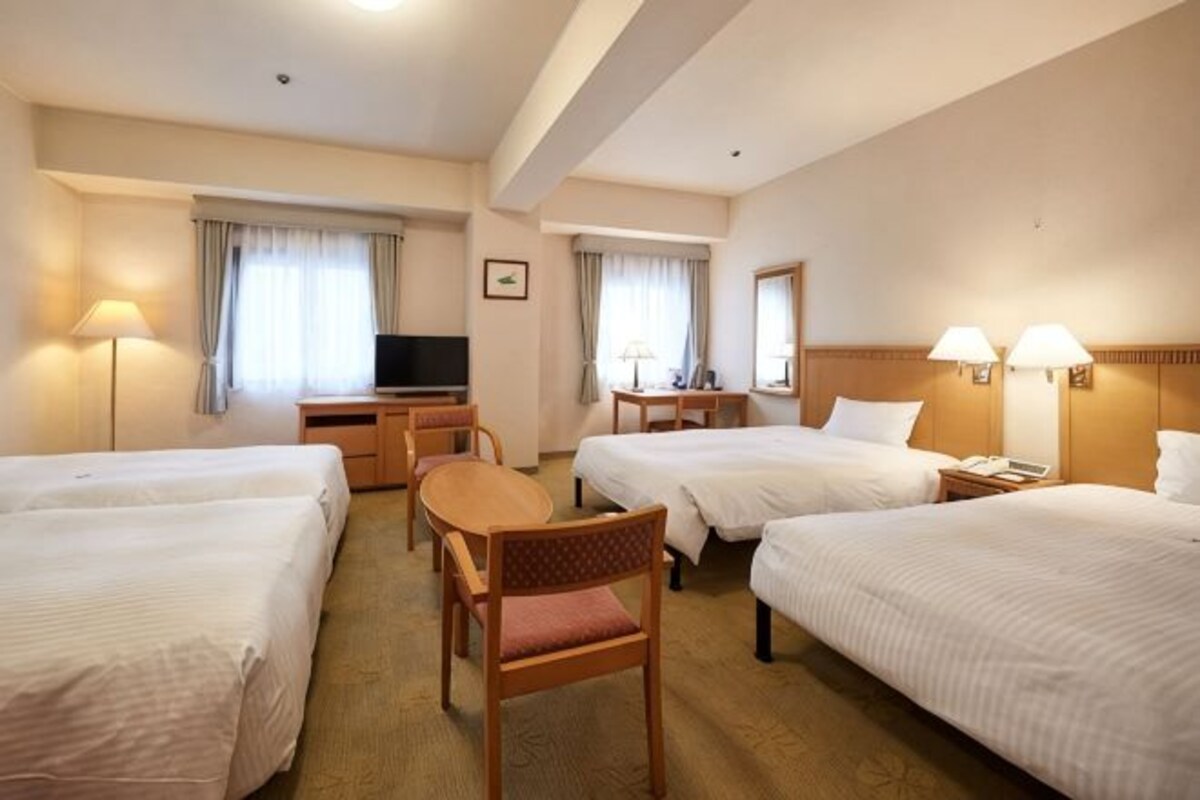 Una habitación de hotel con cuatro camas, un escritorio, un televisor y dos lámparas.