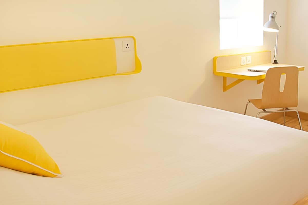 A room with a bed, a desk, a chair, and a lamp.