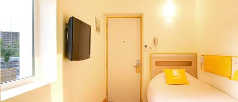 A hotel room with a bed, a television mounted on the wall, a door, and a window.