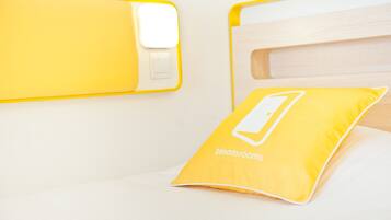 A bed with a yellow pillow labeled "bloomrooms" and a bedside table with a white lamp.