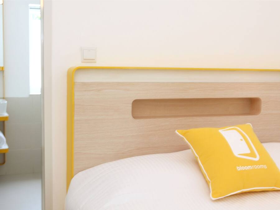 Uma cama com cabeceira de madeira e um travesseiro amarelo com a inscrição bloomrooms.