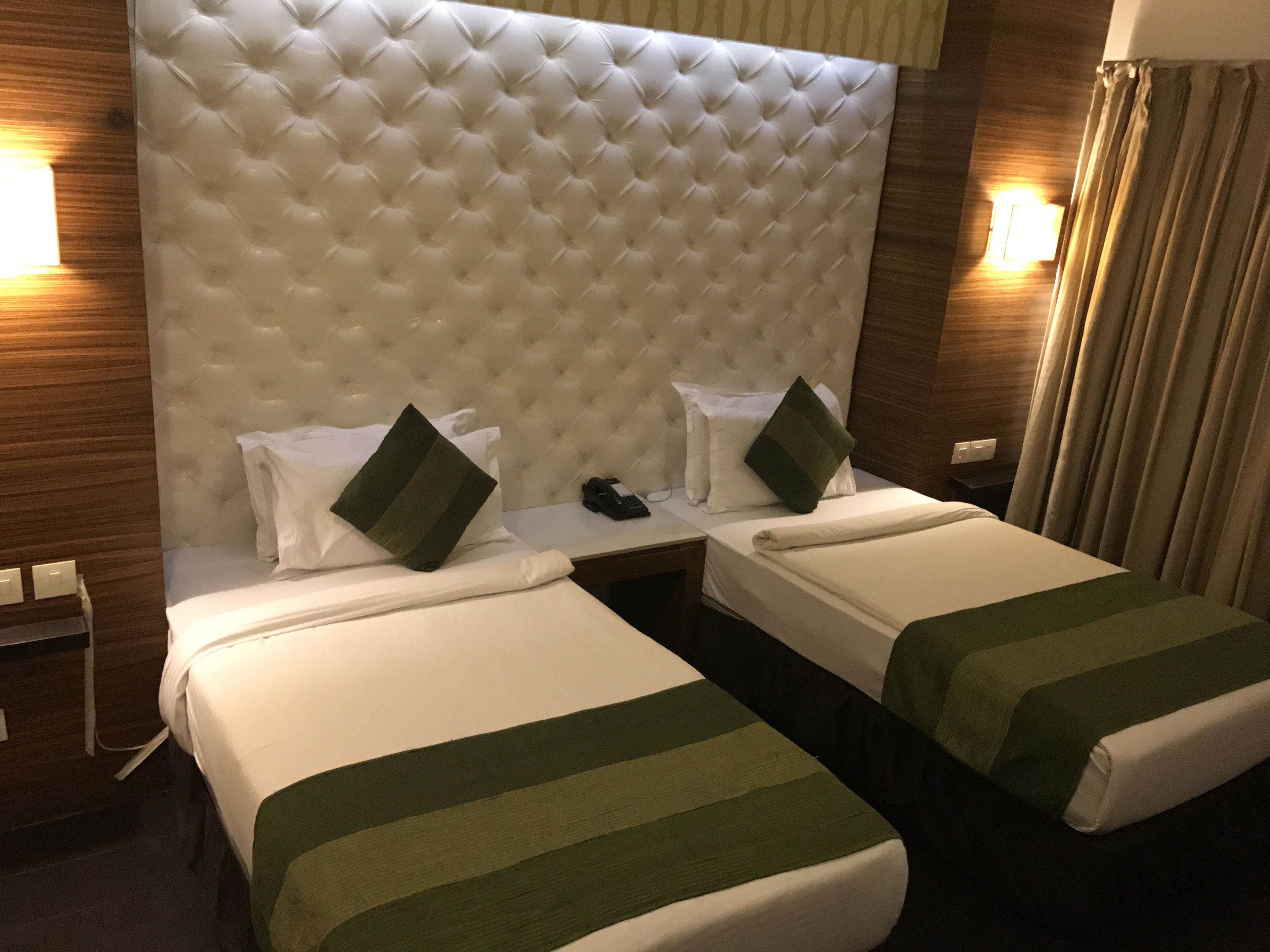 Une chambre d’hôtel avec deux lits, une tête de lit capitonnée, des tables de chevet et des lampes.