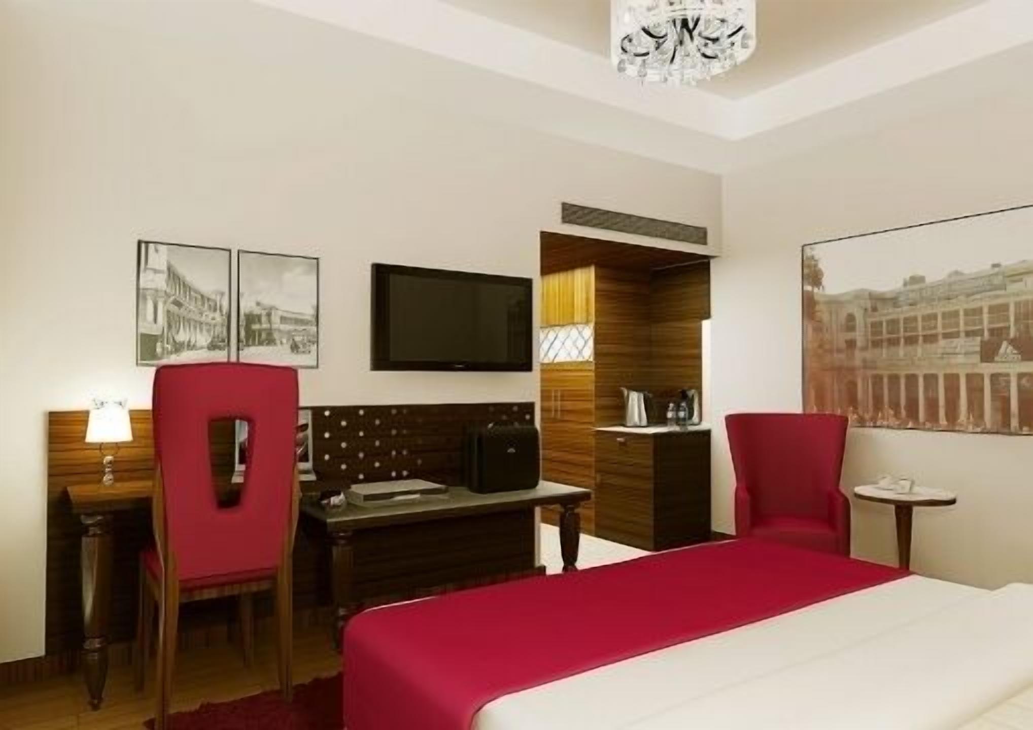 A hotel room with a bed, a desk, a chair, a TV, and a painting on the wall.