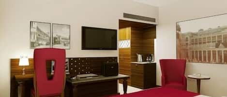 A hotel room with a bed, a desk, a chair, a TV, and a painting on the wall.