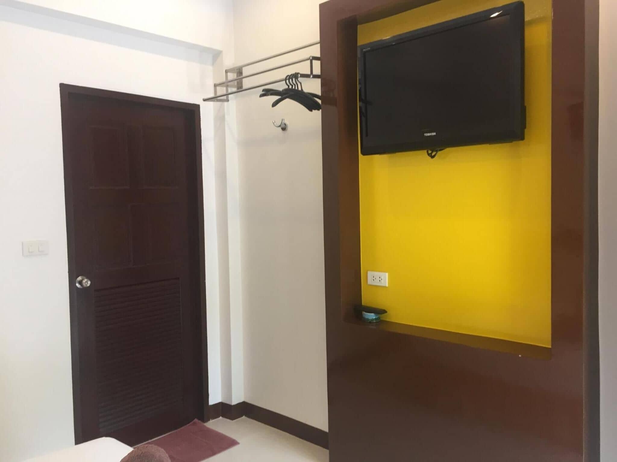 Une pièce avec une porte en bois foncé, un mur jaune et un téléviseur à écran plat fixé au mur.
