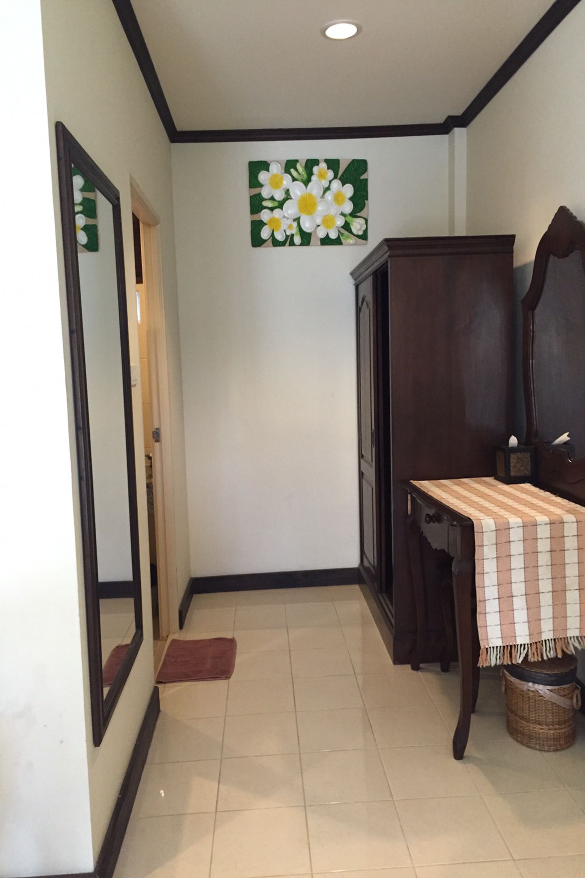 A hallway with a mirror, a wooden cabinet, a table with a checkered tablecloth, and a floral wall decoration.