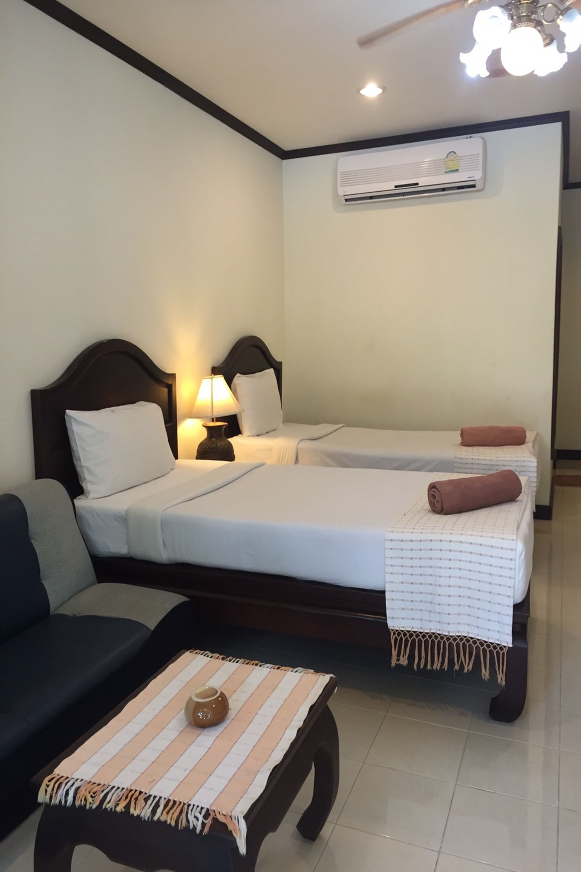 Une chambre d’hôtel avec deux lits, un canapé, une petite table avec un vase et un ventilateur de plafond.
