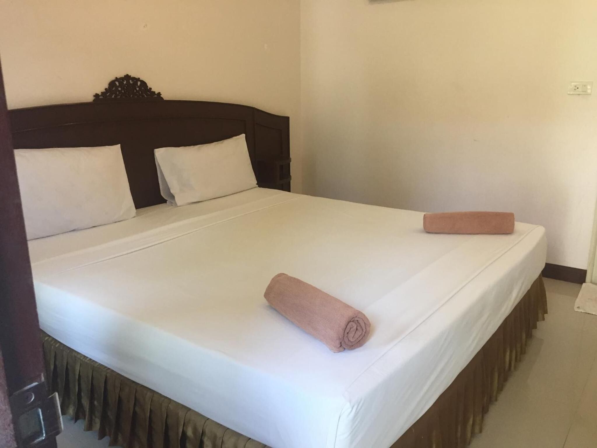 Un lit bien fait, avec du linge de lit blanc et deux serviettes roses, une tête de lit en bois et une décoration simple et épurée.