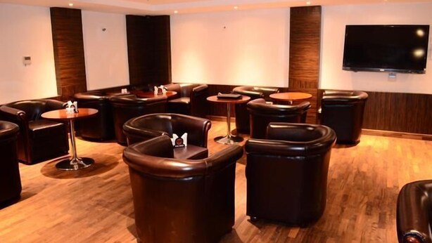 A room with leather sofas and round tables, a flat-screen TV mounted on the wall, and a wooden floor. - BKR Grand (Chennai)