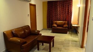 A living room with a brown leather sofa, a matching armchair, and a small wooden coffee table. - BKR Grand (Chennai)