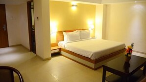 A hotel room with a bed, bedside lamps, a small table with a vase, and a ceiling fan. - BKR Grand (Chennai)